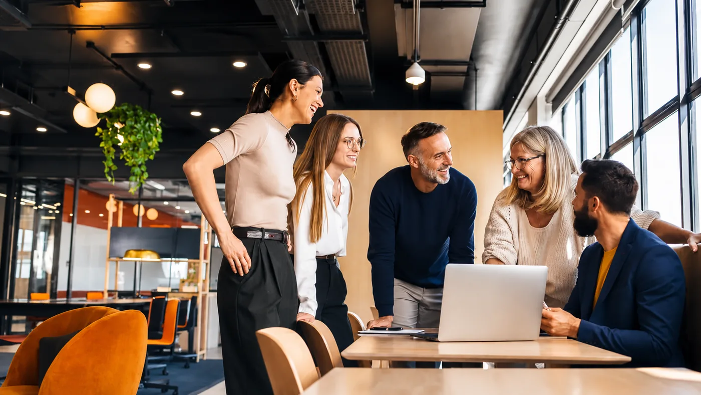 Fünf Personen besprechen ein Projekt am Laptop in einem hellen Büro